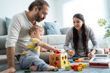 Beyaz, mutlu bir ebeveyn, bebek bebekle oturma odasında oynuyor. Çekici bir çift anne ve baba evde küçük bir çocukla vakit geçiriyor. Ev kavramında etkinlik ilişkisi.