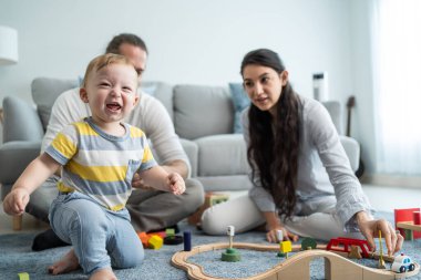 Beyaz, mutlu bir ebeveyn, bebek bebekle oturma odasında oynuyor. Çekici bir çift anne ve baba evde küçük bir çocukla vakit geçiriyor. Ev kavramında etkinlik ilişkisi.