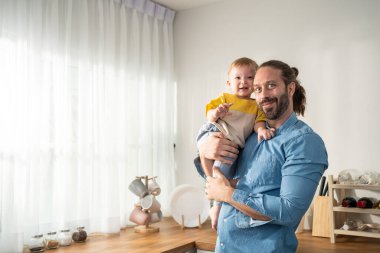 Portrait of Caucasian loving father hold baby boy child in living room. Happy family, attractive caring young dadd carry his toddler son on hands with happiness in house. Activity relationship at home
