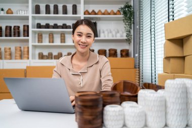 Portrait of Asian woman sell vase product online and looking at camera. Attractive young businesswoman using laptop computer checking sale order and feel happy with financial of business in warehouse.