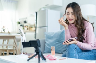 Asyalı profesyonel kadın sanatçı evde kalıp makyajın keyfini çıkarıyor. Çekici, güzel bir kız kanepeye oturur, mutlu bir şekilde aynaya bakar ve yüzünü boyayan kaşlarla evin güzelliğinin tadını çıkarır..