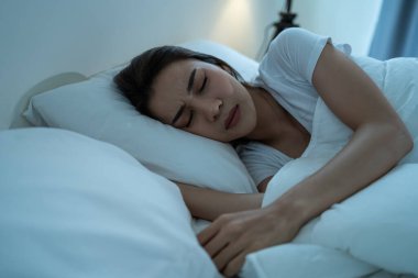 Asian beautiful woman lying down on bed in bedroom, dreaming at night. Attractive young female in pajamas sleeping alone on comfortable pillow and cozy blanket in dark room for health care at home.