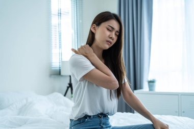 Asian beautiful sick girl in pajamas getting up from sleep in bedroom. Unhappy young woman feel bad and painful after wake up on bed, having backache then press hands to massage lower back at night.