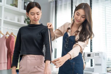 Asian tailor woman measure customer's body to making her new clothes. Attractive female fashion designer dressmaker working and design new fashion collection for customer in tailoring atelier workshop