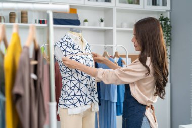Asian beautiful tailor woman working on clothes in tailoring atelier. Attractive young girl fashion designer use tape measure new handmade suit on mannequin in workshop room. Fashion business concept.