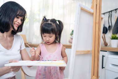Asian young happy kid daughter coloring on painting board with mother. Happy family activity, Little girl child learn how to draw art picture with watercolor paint and brush enjoy creativity with mom.