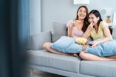 Asyalı güzel lezbiyen kadın çift evde birlikte TV izlemekten hoşlanıyor. Çekici iki eşcinsel arkadaş oturma odasında kanepede oturur ve televizyonda mutlu bir film izlerler. Homoseksüel-LGBTQ kavramı.