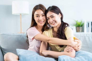 Portrait of Asian beautiful lesbian woman couple smile, look at camera. Attractive two female gay friend sit on sofa, spending leisure time together in living room in house. Homosexual-LGBTQ concept.