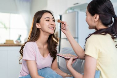 Asian beautiful lesbian woman couple enjoying makeup together in house. Attractive two female gay friend sit on sofa in living room, feel happy for beauty cosmetic at home. Homosexual-LGBTQ concept.