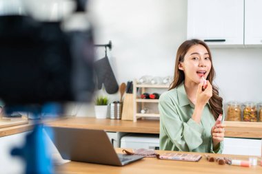 Evdeki kozmetiği incelemek için kamerayla Asyalı kadın video blogcu konuşması. Güzel blogcu Nüfuzlu Kız kanepeye oturur ve canlı yayında izleyicilere makyaj malzemelerini gösterir..