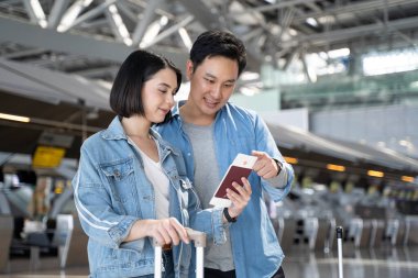 Asian young new marriage couple passengers walking in airport terminal. Attractive man and woman tourist enjoy travel for holiday honeymoon trip and walk from boarding gate to airport transportation.