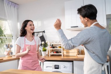 Asian attractive loving couple enjoy dance together in kitchen at home. Beautiful romantic new marriage man and woman wear aporn feeling happy and enjoy activity relationship in house listen to music.
