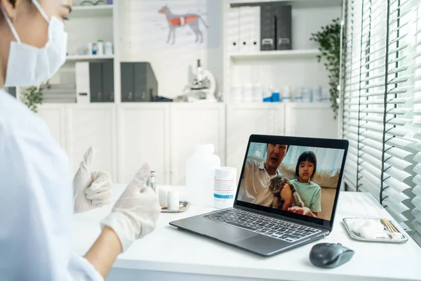Asian veterinarian girl talk to pet owner on online virtual video call. Professional vet doctor woman use laptop computer to give treatment plan consult for little cat animal while sit in pet hospital