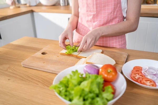 Close up of attractive woman making sandwich for breakfast in morning. Beautiful girl wear apron enjoy eat clean vegetables healthy food for health care in house. Diet lose weight and foods concept.