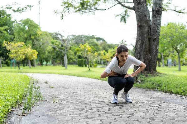 Asian attractive sport woman feels pain on stomach after run on street. Beautiful girl in sportswear having stomach ache illness while exercise by jogging workout outdoor in the evening in public park