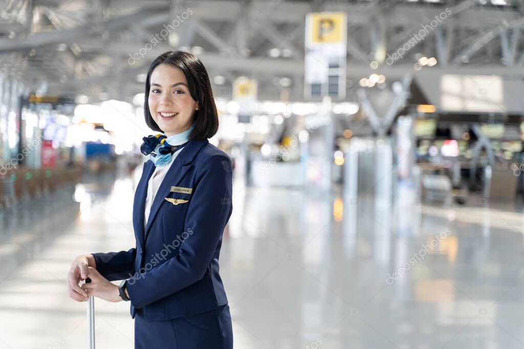 Portrait of Caucasian flight attendant standing in airport terminal. Attractive beautiful cabin crew or air hostess woman smiling and looking at camera with confidence before walk to airplane for work