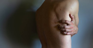 Kaşındırıcı ürtiker semptomları olan bir adam. Sırtını kaşıyan bir adam var. Gri arka planda tek başına.
