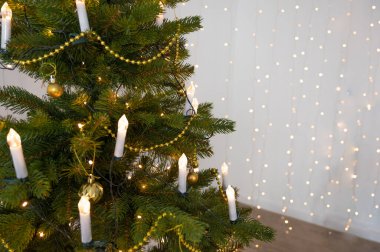 Yılbaşı ağacı, mum ampulleri ve beyaz duvardaki ışıklarla kopyalama alanı.