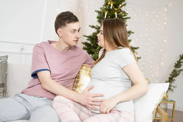 Marito prendersi cura della sua incinta, accarezzando la pancia sopra sfondo albero di Natale — Foto Stock