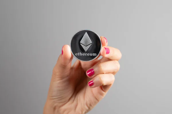 Moeda de prata Ethereum em uma mão das mulheres sobre fundo cinza. Criptomoeda Blockchain. Moeda virtual Money.Crypto Fotos De Bancos De Imagens