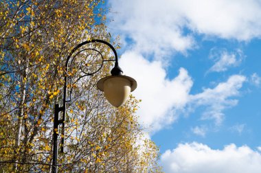 Sonbahar ağaçlarına karşı fener. Sonbahar parkındaki sokak lambası. Eski moda lambalı sonbahar manzarası.