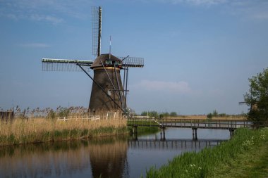 Hollanda Kinderdijk 'teki tarihi yel değirmeni ahşap bir köprünün geçtiği kanalın kenarındaki sazlıklarla çevrili..