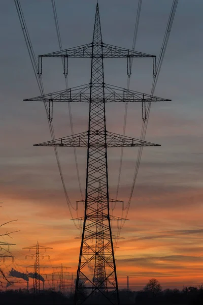Yüksek voltajlı elektrik hatları ve pilonların silueti gün batımından sonra renkli bir gökyüzünün önündeki buhar santraline çıkıyor. Karlsruhe, Almanya