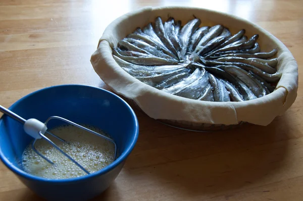 Zubereitung von Kuchen (Teig und Fisch in eine gläserne Auflaufform, in der Nähe einer Tasse mit geschlagenen Eiern) — Stockfoto