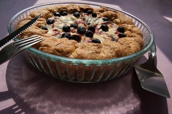 Torta in un piatto di vetro sul tavolo, vicino a coltello, forchetta e pagaia per pia, macro . — Foto Stock