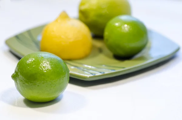 Citrons et limes sur une assiette verte, fond flou — Photo