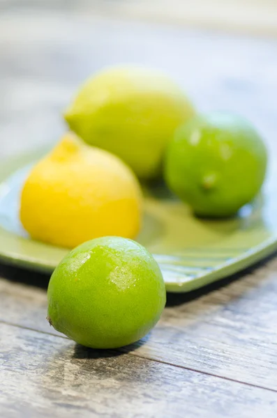 Citrons et limes sur une assiette verte, fond flou — Photo