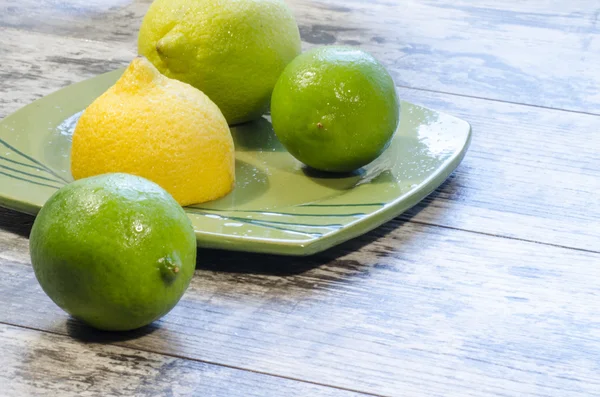 Citrons et citrons verts sur une assiette verte — Photo