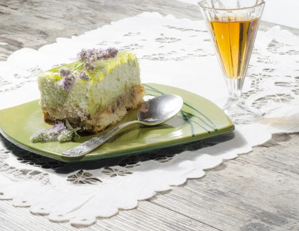 Slice of lime cheesecake decorated with mint flowers and glass of cognac — Stock Photo, Image