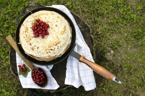 Pancakes with red currants on old pan and wooden spoon — Stock Photo, Image
