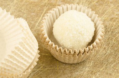 Beyaz, yuvarlak, Hindistan cevizi, çikolata terlemeleri ve altın zemin üzerine kağıt ambalaj