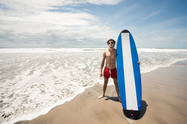 Starker junger Surfer am Strand mit einem Surfbrett. ba — Stockfoto