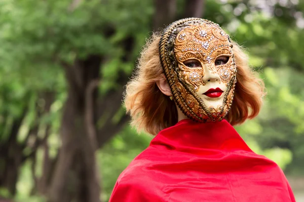 Blonde vrouw in carnaval masker over gebladerte achtergrond — Stockfoto