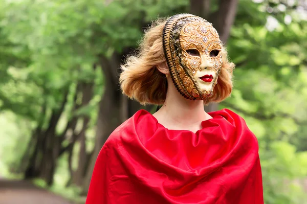 Blonde vrouw in carnaval masker over gebladerte achtergrond — Stockfoto