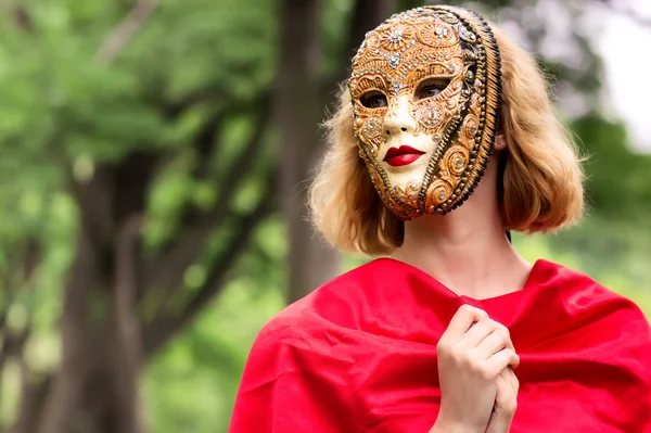 Blonde vrouw in carnaval masker over gebladerte achtergrond — Stockfoto