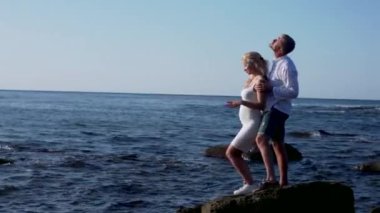 Hamile kadın ve erkek denizin kayalıklarında dikiliyorlar.