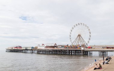 Turistler Blackpool sahilindeki basamaklarda oturmuş Eylül 2021 'de Central Pier' de dönen dönme dolabı izliyorlar..