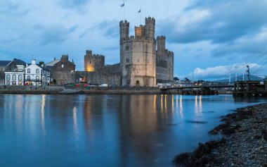 Caernarfon Şatosu, Ekim 2021 'de alacakaranlıkta Kuzey Galler kıyısındaki ufuk çizgisi ve rıhtımına hakimdir..