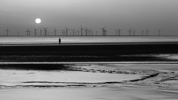 黑白照片上 一个钢铁人看着太阳落山在Burbo Bank风电场外的Crosby海滩 这是安托尼 高姆利四月在利物浦附近拍摄的另外一座雕塑 一百座铁人雕像中的一座 — 图库照片