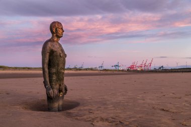 Eylül 2021 'de Liverpool yakınlarındaki Crosby plajında bir Demir Adam' ın üzerindeki bulutlar pembe ve öğrenci ışığıyla parladı. Antony Gormley tarafından Sefton kıyı şeridini işgal eden 100 Demir Adam heykelinden biridir..