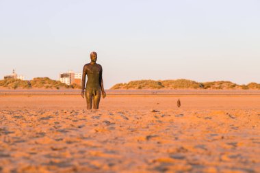 Liverpool yakınlarındaki Crosby plajındaki 100 Demir Adam heykelinden ikisi, Antony Gormley tarafından yaratılan başka bir yeri oluşturur. Bu, 2021 Nisan 'ında gün batımında, gezinti güvertesine bakarken çekildi..