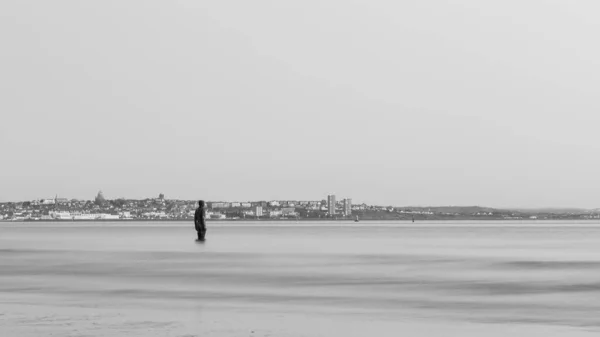 一个黑白相间的铁人出现在维拉尔半岛前这是另一个地方的一部分 在利物浦附近的克罗斯比海滩上的艺术装置 由安东尼 高姆利 Antony Gormley 创作的100尊钢铁人雕像组成 这是四月日落时捕捉到的 — 图库照片