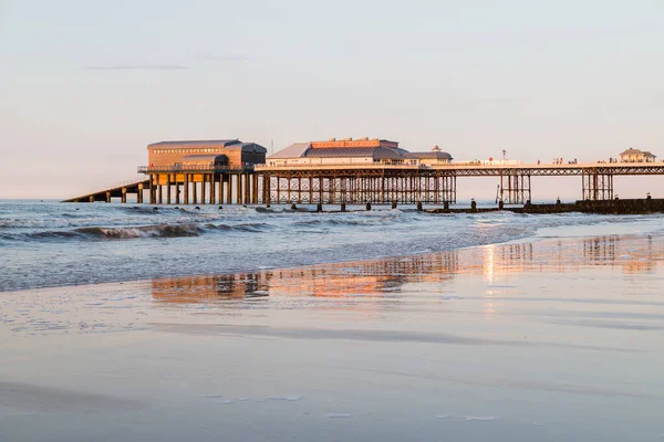 2021 Haziran 'ında gün batımında batımında, güneş kumlu plajı aydınlatırken batıdan Cromer iskelesi görüldü..