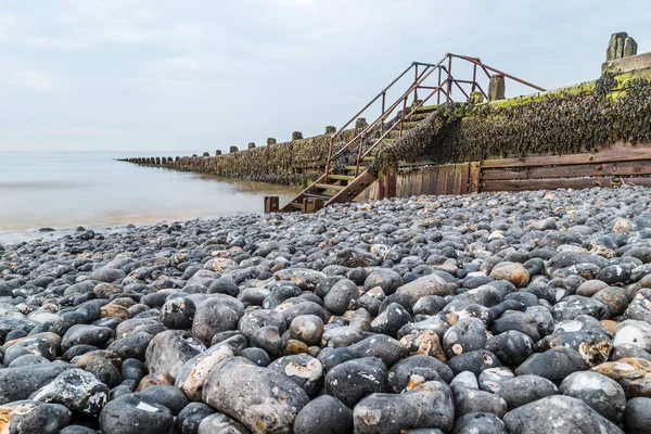 Long exposure of the waves lapping up to the large pebbles on Cromer beach on the North Norfolk coast.  The large groynes are so tall in places that wooden steps are needed to walk over them.