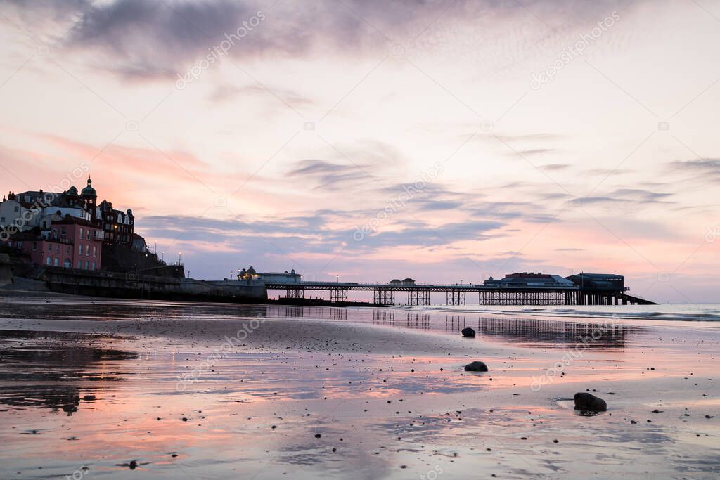 Colourful reflections of Cromer pier seen in the wet sand at low tide during dusk one evening in June 2021 on the North Norfolk coast.