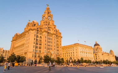 İnsanlar Ağustos 2021 'de Liverpool rıhtımındaki Three Graces' in önünde kaykay kayarken yaz güneşinin tadını çıkarıyorlar..